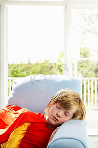 小男孩(7-9岁)在室内穿着超级英雄服装睡在扶手椅上