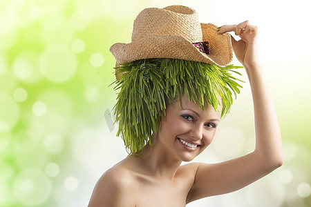 青草背景摄影照片_漂亮的年轻女子，戴着夏日帽子，留着发型，在颜色的背景上带着一些青草微笑