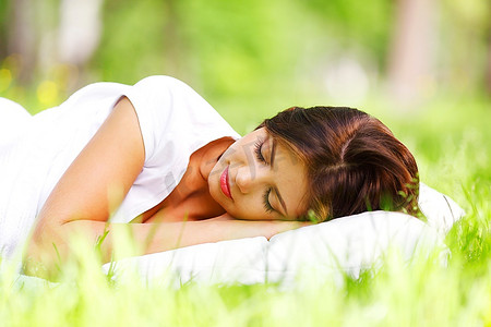 睡觉的枕头摄影照片_睡在柔软的枕头上的年轻女子，睡在新鲜的春草中