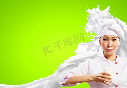 飞溅水花摄影照片_亚洲女厨师手持一杯牛奶，穿着红色围裙，手持牛奶，在彩色背景下飞溅