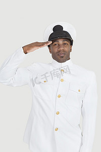 自信的年轻非裔美国海军军官在灰色背景下敬礼的肖像