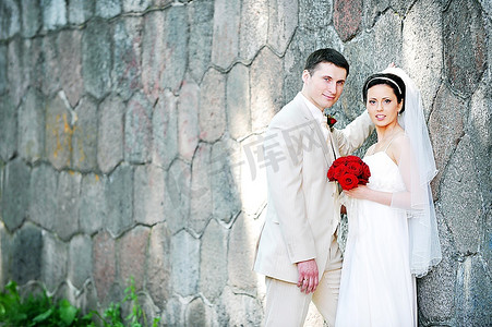 穿着白色礼服的新娘和新郎在老墙附近