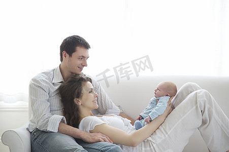 一家三口抱着两周大的新生儿坐在沙发上