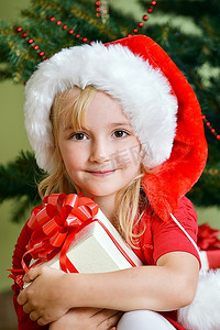 圣诞帽绿色摄影照片_圣诞树附近戴着圣诞帽的漂亮小女孩