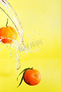 两个橘子和水溅在黄色上，特写