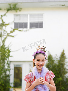 女孩皇冠摄影照片_女孩(10-12岁)戴着皇冠，戴着羽毛围巾站在屋外