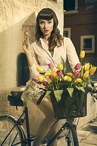 可爱的黑发美女喜欢复古时尚美女坐在自行车上，带着五颜六色的花篮和老比赛