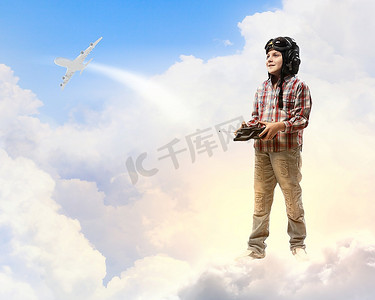戴着飞行员头盔的小男孩在云的背景下玩玩具无线电飞机