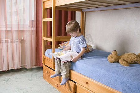 5岁男孩坐在双层床上看书