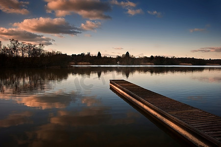 平静的江水摄影照片_晚霞在平静的湖面上的美丽景象，长长的钓鱼码头和鲜艳的色彩