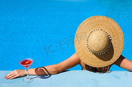 戴着帽子的女人在泳池边放松，喝着国际化的鸡尾酒