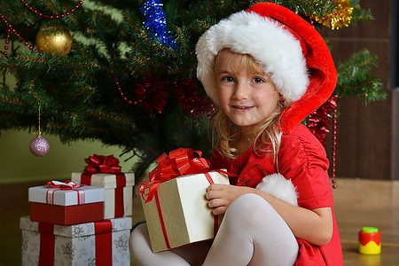 漂亮的小女孩在圣诞树附近的圣诞帽