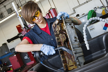 机械零件摄影照片_汽车修理厂用焊枪在汽车机械零件上工作的年轻女机械师
