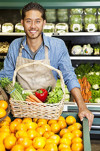 画象一个快乐的人与菜篮子站在附近的橘子摊位在超市