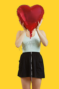 一名年轻女子躲在黄色背景上的心形气球后面