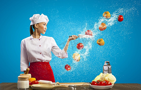 刀切水果摄影照片_亚洲女厨师在空中用刀切水果和蔬菜