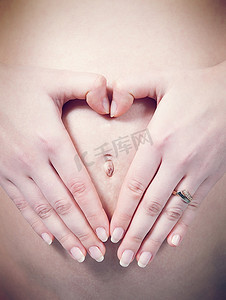 特写手指在怀孕的白人妇女的肚脐上心形；急性；S腹部。孕期收藏。