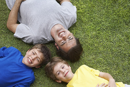 父亲和两个儿子（6-11）躺在草地上，从上面看