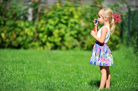 小女孩玩与吹泡泡机在绿色草坪