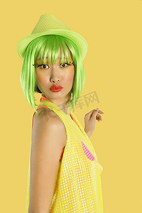 黄色服装背景摄影照片_时髦的年轻女子的肖像，绿色的头发在黄色的背景下皱起嘴唇
