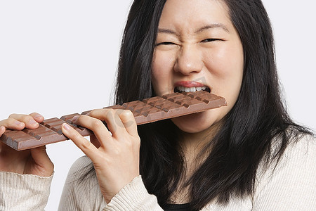 一名年轻女子在浅灰色背景下吃着一块大巧克力的肖像