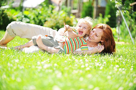 年轻漂亮的母亲带着女儿在草地上玩耍。夏天。