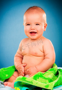 婴儿洗浴摄影照片_在蓝色背景上的绿色毛巾的愉快的小婴孩。