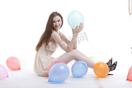 美丽的年轻女子穿着连衣裙躺在地板上，白色背景上有气球