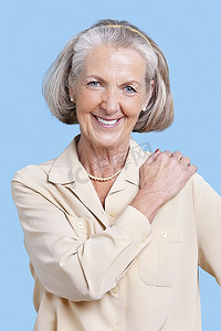 微笑的老年妇女身着便装，手放在肩上，蓝色背景