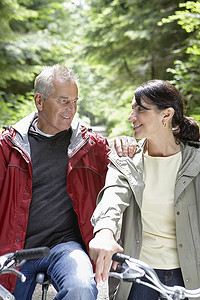 年长的男人和中年女人在森林里骑自行车，微笑着
