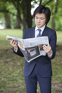 年轻的商人读报纸在公园