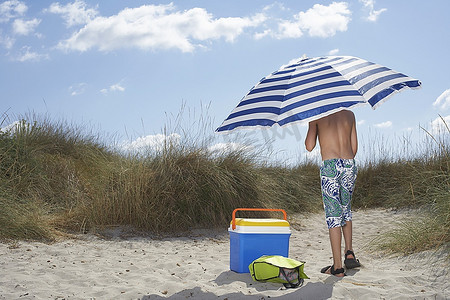 男孩(10-12岁)撑着伞站在海滩上，背影
