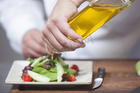 中年厨师将橄榄油浇在配菜沙拉上