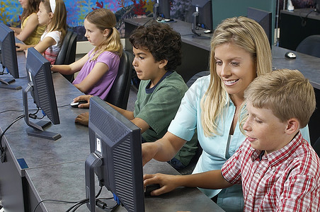 小学生在教室里和老师一起使用电脑