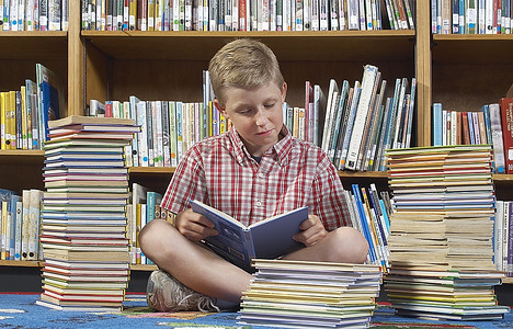 坐在地板上在图书馆看书的男孩