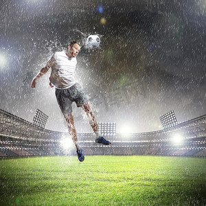 雨中的人摄影照片_在雨中的体育场用头击球的白色衬衫的足球运动员