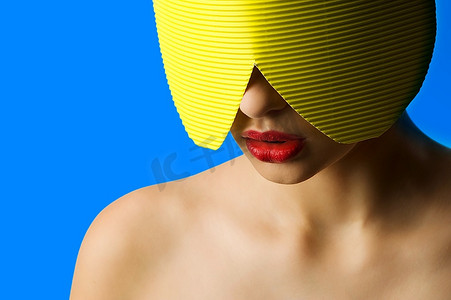 一位年轻女子的时尚肖像，戴着黄色纸面具，蓝色背景上有红色的嘴唇