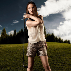 性感的女人在闪闪发光的短裤和hig鞋打高尔夫球，她需要的高尔夫俱乐部与右手附近的右肩，并期待在镜头