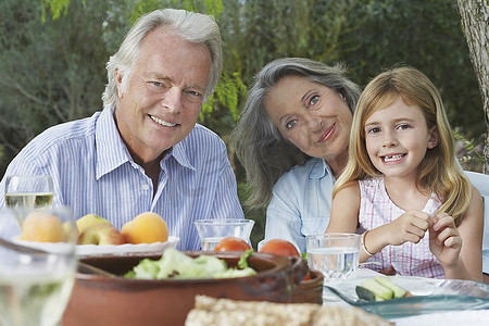 祖父母和孙女(5-6岁)坐在花园的桌子旁，肖像