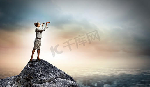 人望远镜摄影照片_站在岩石顶上用望远镜看的女商人形象