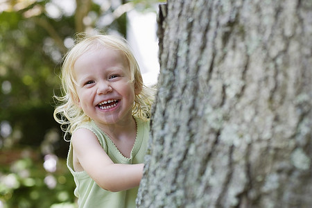 肖像的年轻女孩（1-2）偷看从后面的树，笑