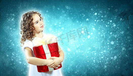拿着圣诞节礼物，与圣诞节光bokeh的黑暗背景的一个逗人喜爱的年轻女孩