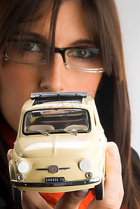 戴着眼镜的年轻黑发女郎展示了一辆菲亚特500车型，一辆老式的意大利风格汽车