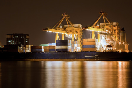 装箱大师摄影照片_有工作起重机的大集装箱货物货船在船厂在晚上为后勤进口出口背景