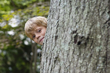 男孩(5-6岁)微笑着从树后偷看的肖像