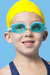 在蓝色背景上，一个戴着泳帽和护目镜的快乐女孩的特写肖像