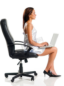 性感的女人，穿着灰色连衣裙，坐在黑色的椅子上，在笔记本电脑上写字