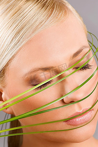 一个金发女孩的美丽的镜头与她的脸周围的一些草叶片。健康理念