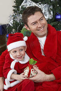戴着圣诞帽的男人抱着男孩(5-6岁)，手里拿着圣诞礼物