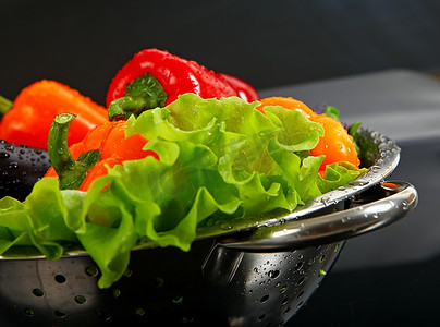 新鲜洗净的新鲜蔬菜在隔绝在黑色背景上的金属滤器中。